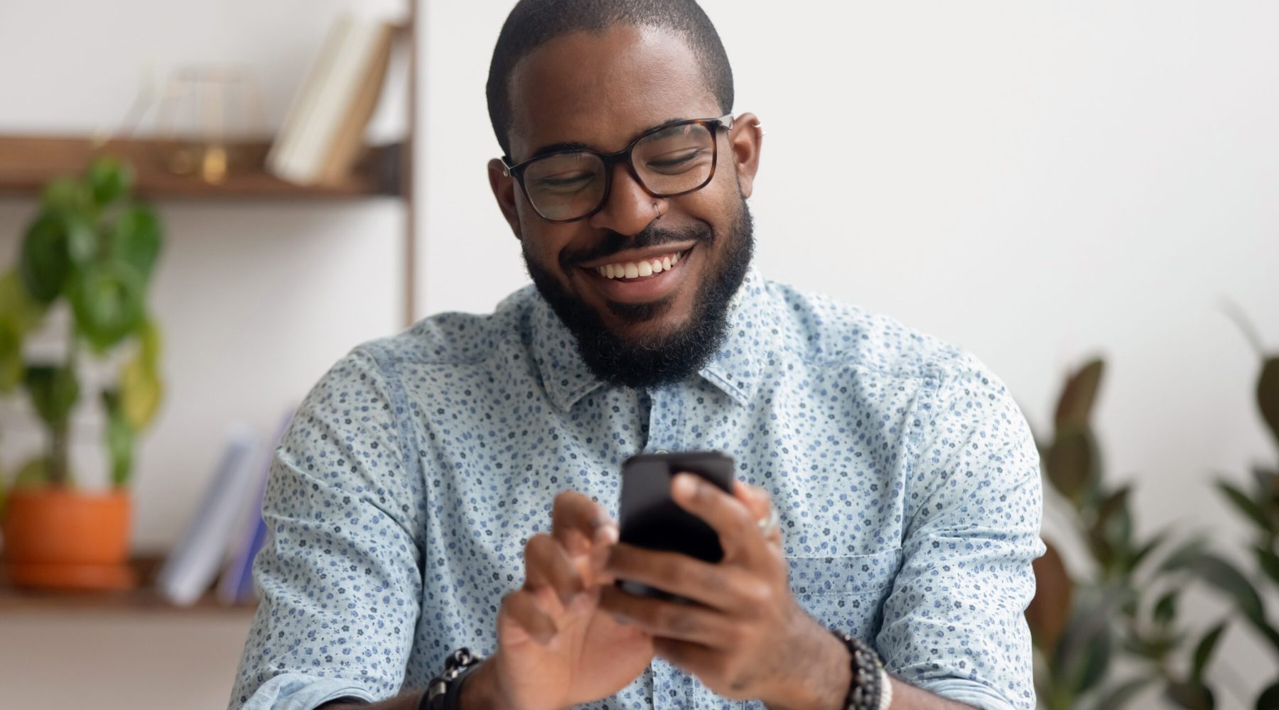 Happy african american businessman using phone mobile corporate apps at workplace texting sms, smiling black man looking at smartphone browsing internet, office technology and digital communication